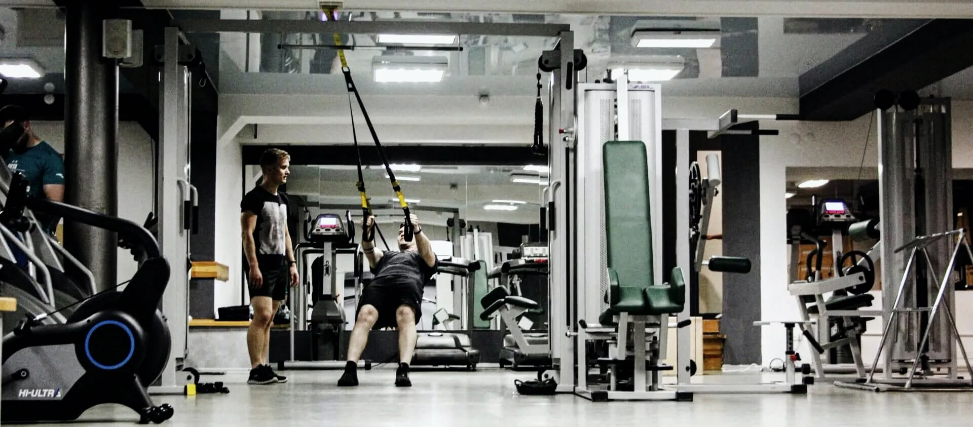 Тренер FitMe поруч із клієнтом на TRX — персональна робота у світлій частині залу